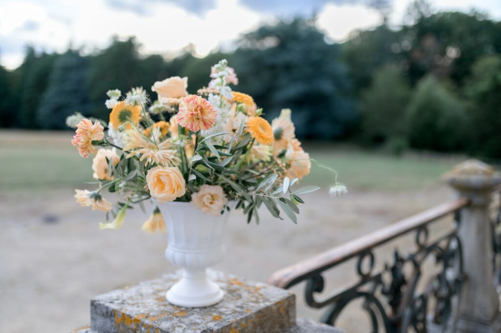 composition florale, se marier dans un château, fleurs de mariage, couleur tendance mariage 2024, abricot , pêche, orange, végétal, vase Médicis
