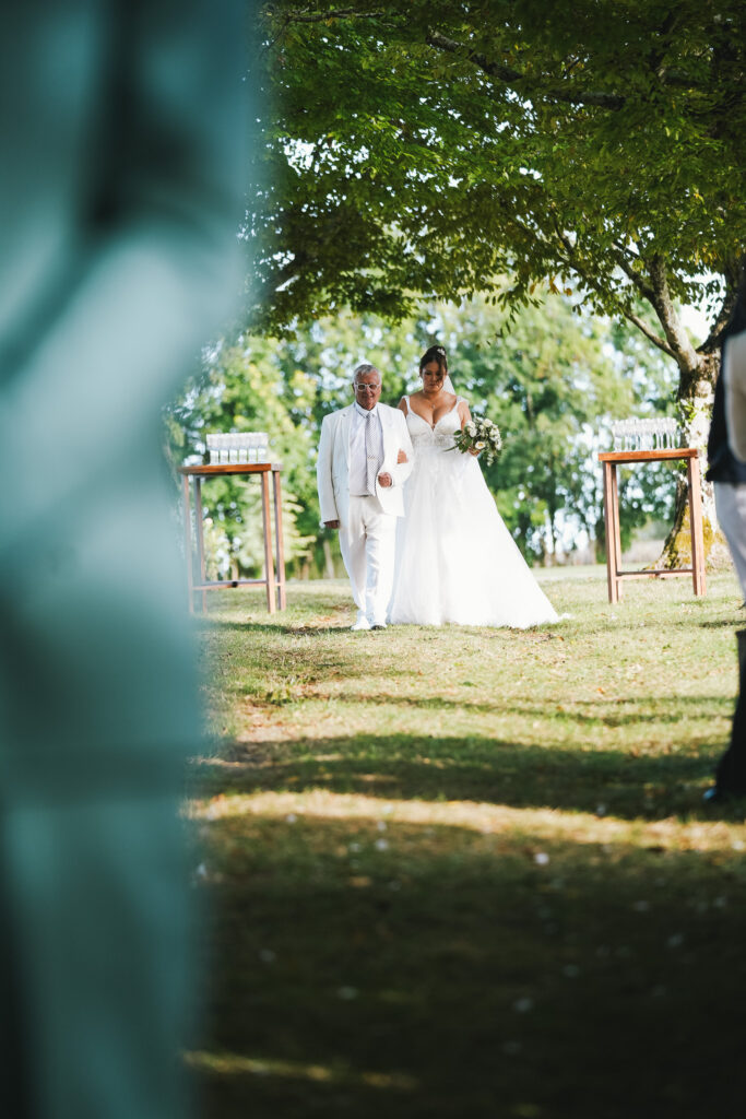 Cérémonie laïque, flou, arrivée mariée, témoin, allée cérémonie, arbre allée cérémonie, cérémonie laique dans la nature, robe de mariée, coupes de champagne, Se marier à Port d'Envaux